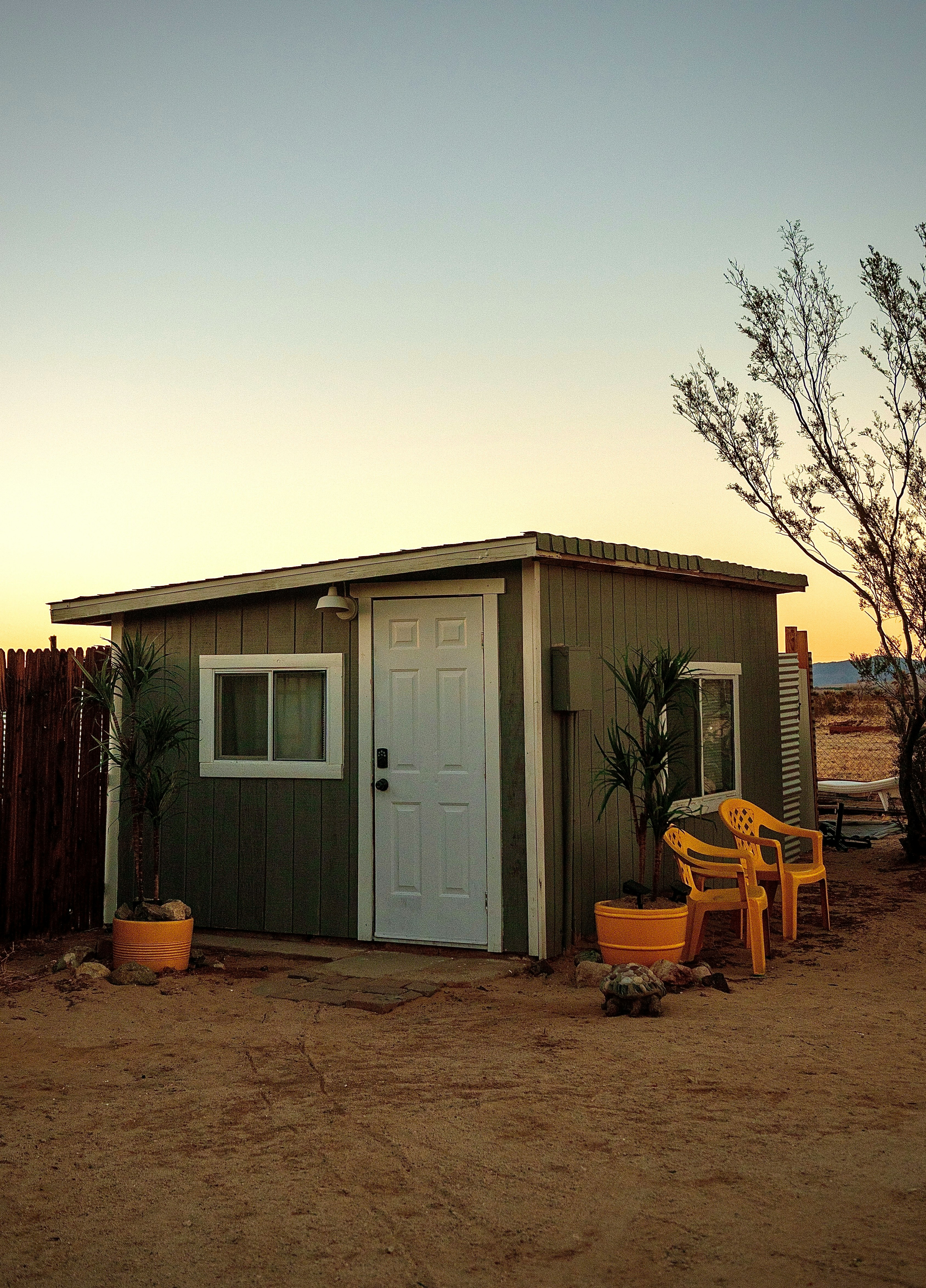 Small detached backyard dwelling at dusk with yellow chairs outside