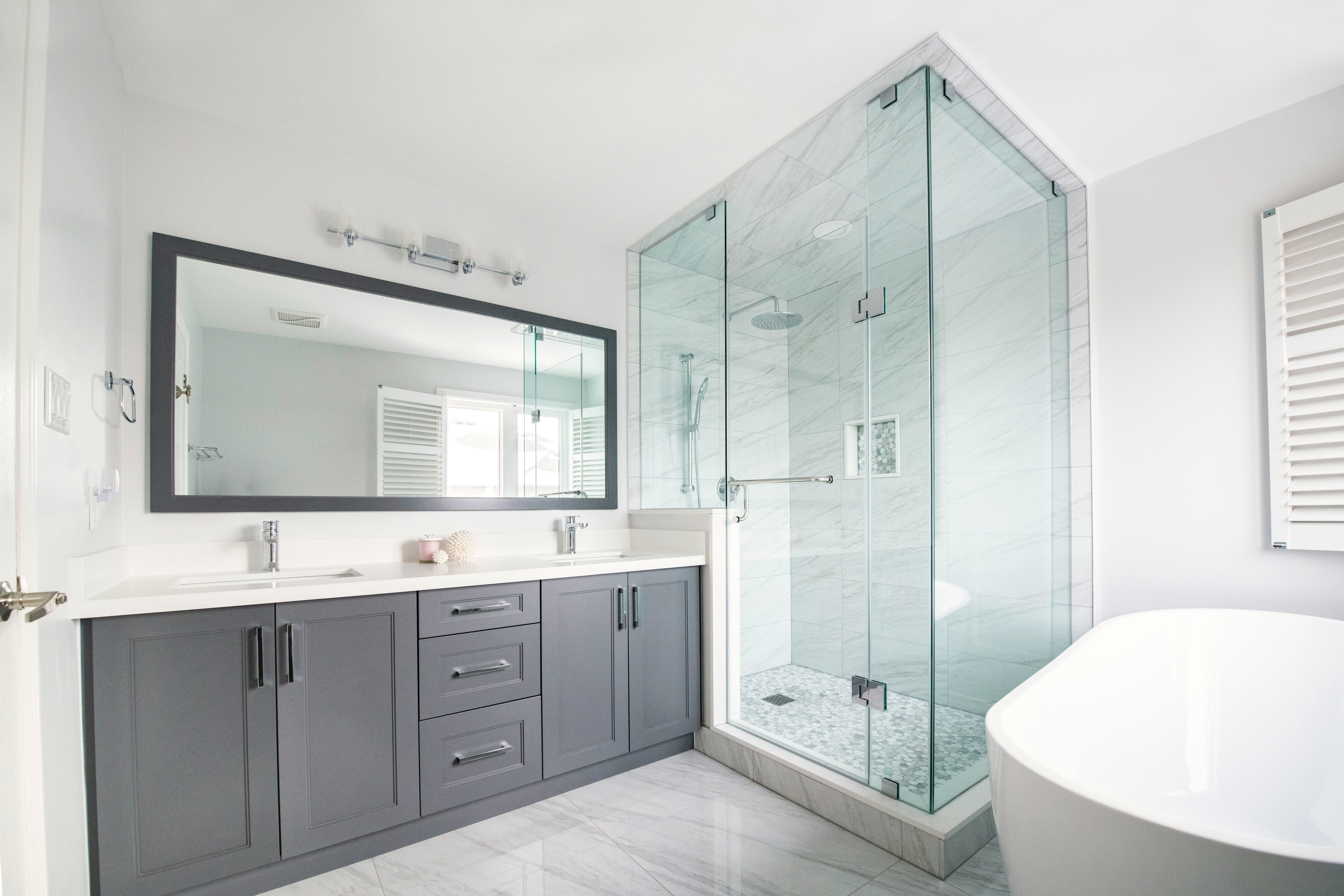 Renovated bathroom with double vanity, glass-enclosed marble shower, and freestanding soaking tub