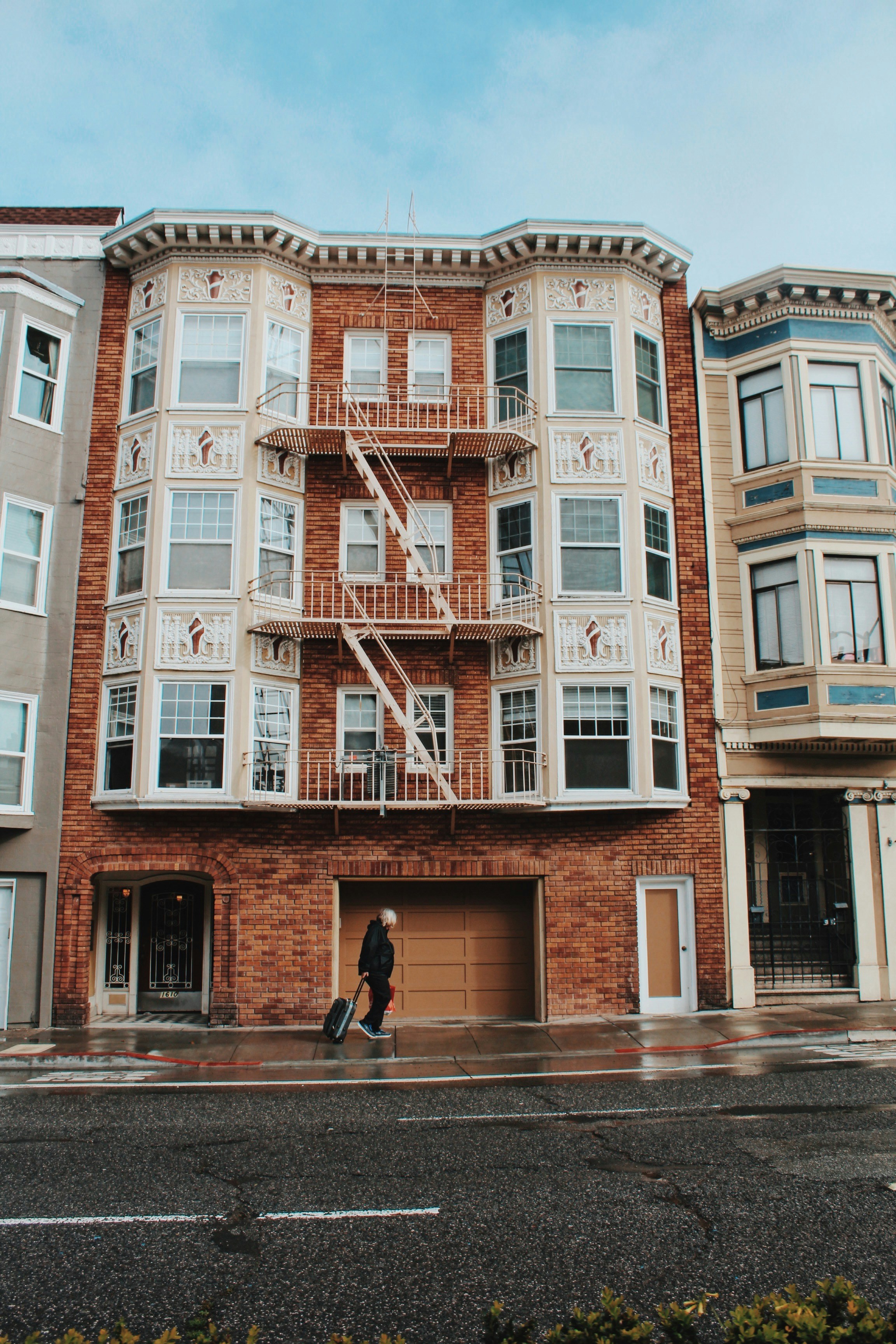 Person walking past a San Francisco residential building with bay windows and a fire escape