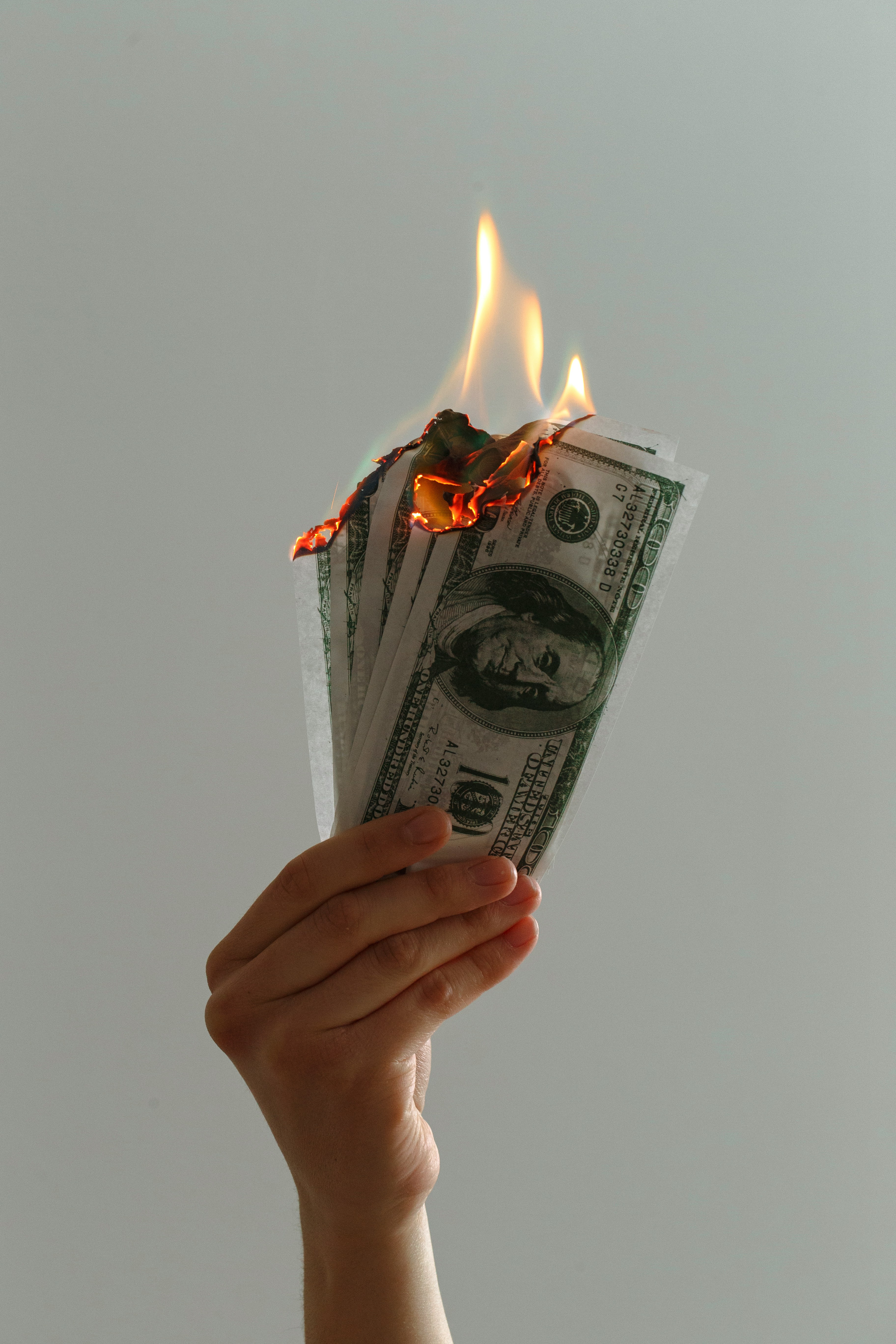 Hand holding burning U.S. dollar banknotes, illustrating the cost of permit delays
