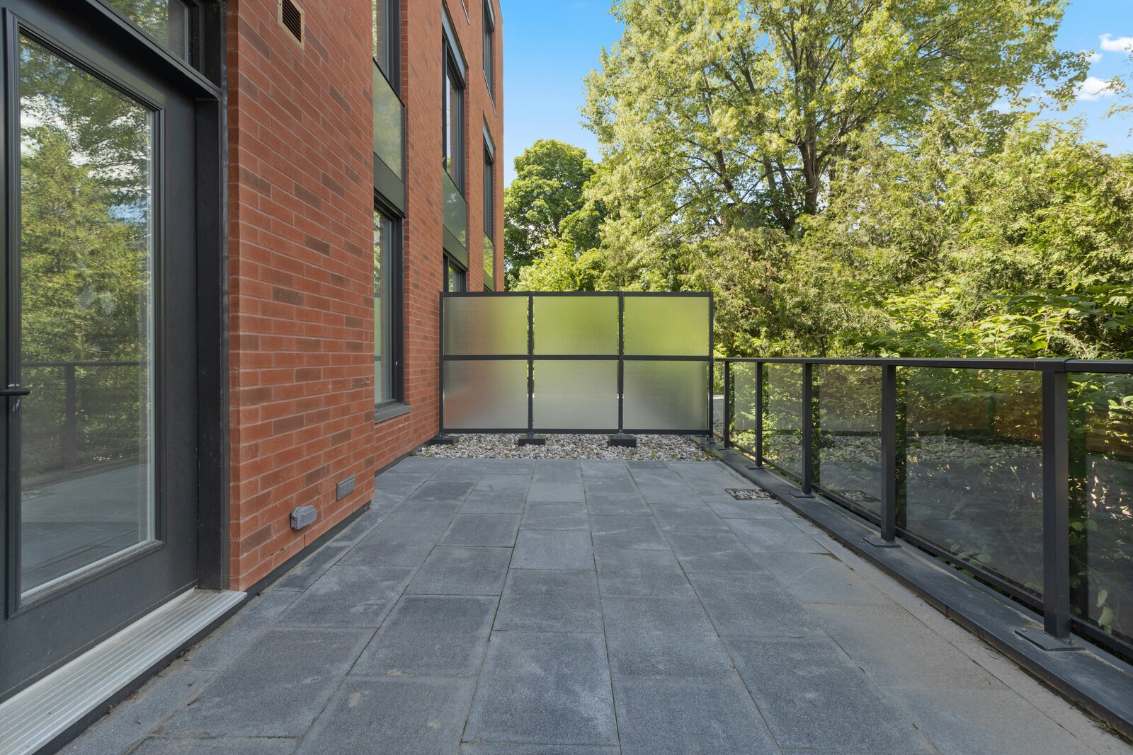 Rooftop terrace with bluestone pavers, a frosted-glass privacy divider, and a black steel railing against a red brick building