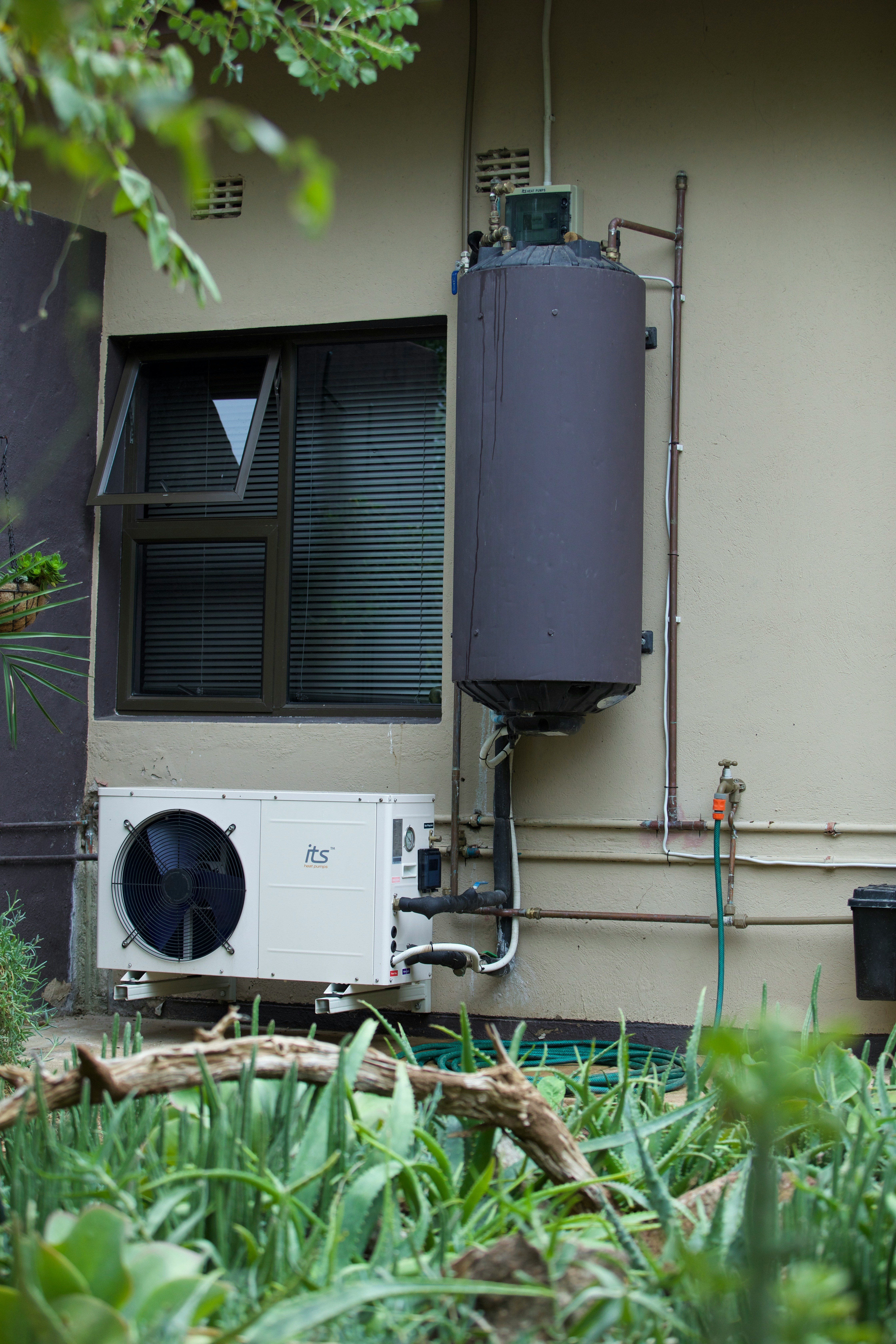 Residential water heater tank and heat pump unit mounted on an exterior wall